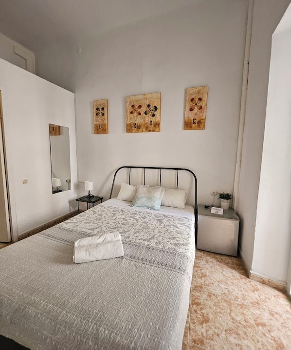 A neatly arranged bedroom with a large bed, bedside tables, a mirror, and three wall art pieces.