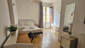 Habitación de hotel con cama, escritorio, silla, mesita, espejo y ventilador de techo.