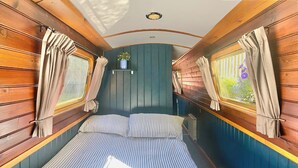 Una cabaña estrecha con una cama individual, ropa de cama a rayas, paredes de madera y cortinas en las ventanas.