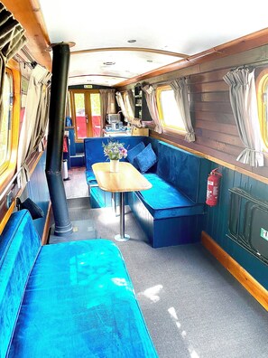A train interior with blue seating, a wooden table, and a small table with a vase of flowers.