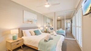 A bedroom with a large bed, bedside tables, a ceiling fan, a large mirror, and a TV on the wall.