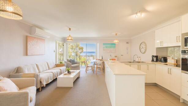 A modern kitchen with a central island, a dining area with a view, and a living room with a sofa and coffee table.