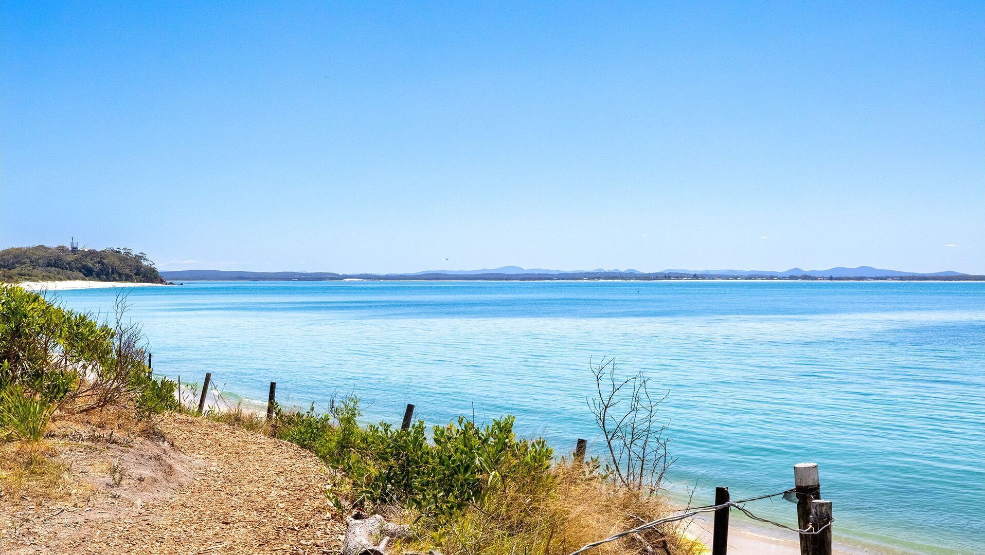 A coastal view with a clear sky, a sandy beach, and a calm sea.