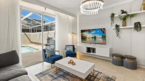 A modern living room with a large TV, comfortable seating, and a view of a pool and outdoor area. - Mickey | Guardians | Pool | Waterpark | Disney 960 (Davenport)