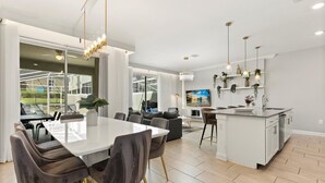 A modern kitchen with a central island, a dining area with a large table and chairs, and a living area with a sofa and TV. - Mickey | Guardians | Pool | Waterpark | Disney 960 (Davenport)