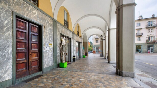 A covered walkway with stone flooring, wooden doors, and green planters. - Apartment 'La Scaletta' with Wi-Fi and Air Conditioning (Biella)