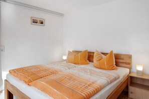 Uma cama com cabeceira de madeira, duas mesas de cabeceira e um criado-mudo com uma lâmpada.
