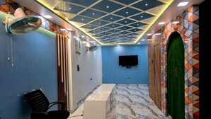 Ein Zimmer mit blauer Wand, einem weißen Empfangstresen, einem schwarzen Stuhl, einer grünen Tür und einer Decke mit geometrischem Muster.