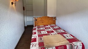 Um quarto pequeno e acolhedor, com cabeceira de madeira, colcha acolchoada e uma luminária de cabeceira.