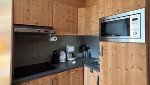 Uma cozinha compacta com armários de madeira, micro-ondas embutido, cafeteira e chaleira.