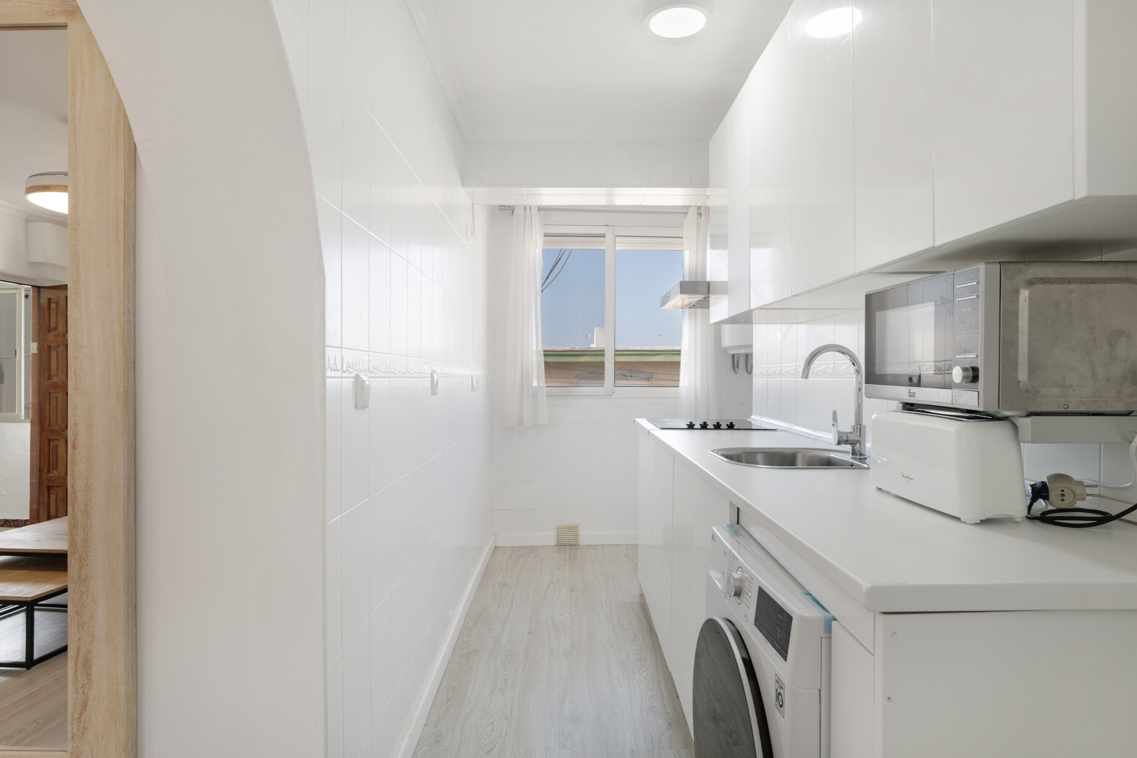 A modern kitchen with white cabinetry, a built-in oven, a microwave, and a sink.