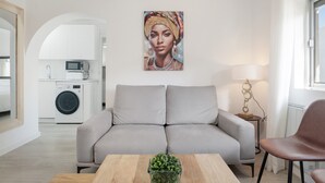 Un salon moderne avec un canapé, une table basse, une lampe et une cuisine en arrière-plan.