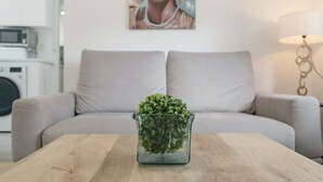 Un salon avec un canapé, une table en verre ornée d’une plante, un tableau au mur et une lampe.