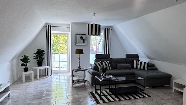 Un salon moderne avec un canapé d’angle, une table basse, une lampe et une vue sur la verdure à l’extérieur.