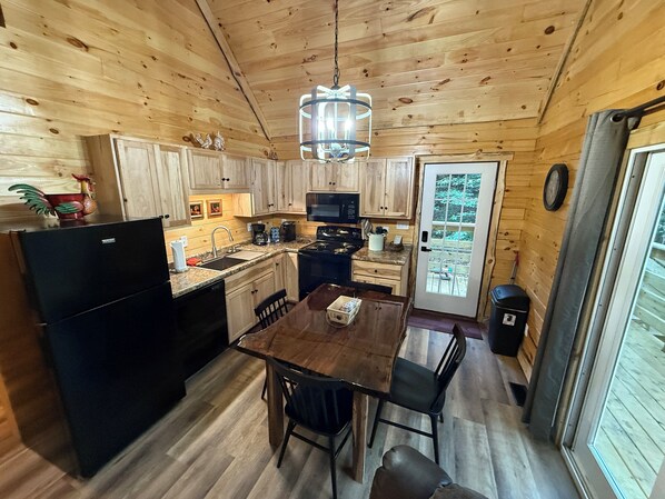 A compact kitchen with wooden cabinets, a black refrigerator, a stove, and a dining table with chairs.