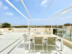 Eine Dachterrasse mit Essbereich, weißen Stühlen, einem Tisch und Blick auf die Stadtlandschaft.