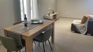 Una sala de estar moderna con una mesa de comedor de madera, dos sillas, un sofá y una mesita auxiliar con un jarrón y una planta.