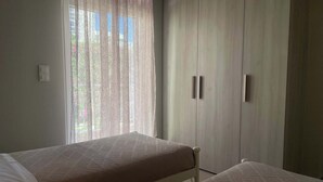 Una habitación con dos camas, un armario y una ventana con cortinas translúcidas.