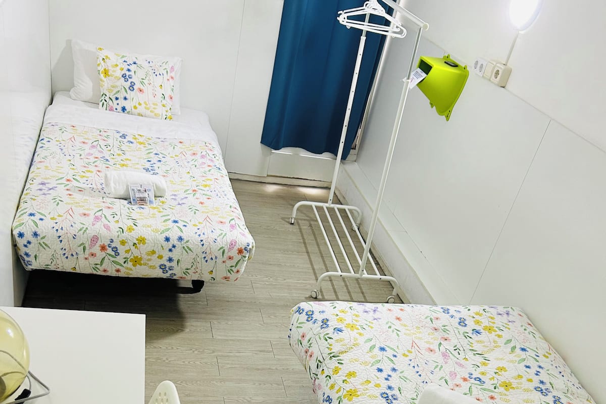 A small, clean room with two single beds, a desk, and a chair.
