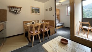 Un coin repas chaleureux, avec des meubles en bois, une table sur laquelle se trouvent un saladier et des verres, et une fenêtre donnant sur l’extérieur.