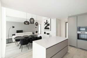 A modern kitchen with a large island, white cabinetry, and a dining area with a black table and chairs.