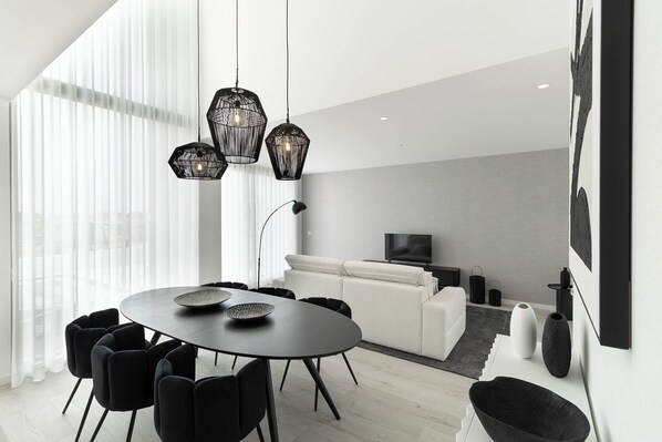 A modern living room with a round dining table, black chairs, a white sofa, and a TV.
