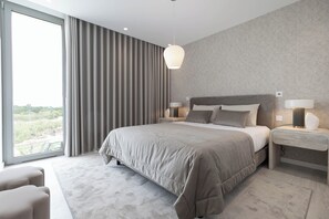 A modern bedroom with a large bed, two bedside tables, and a view of greenery outside.