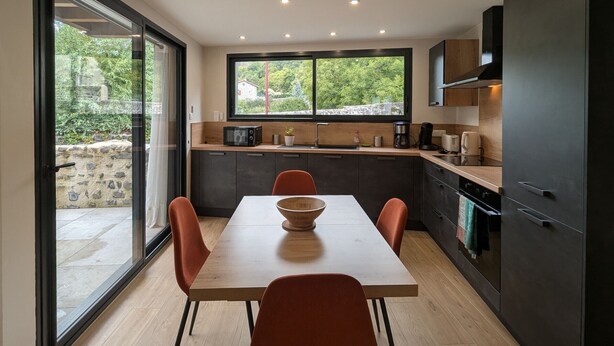 Een moderne keuken met een eettafel, stoelen en uitzicht op groen.