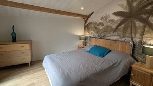 Een slaapkamer met een bed, houten hoofdbord, nachtkastjes, een dressoir en een muurschildering van palmbomen.