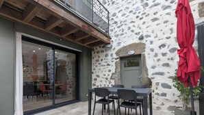 Een buitenmuur van natuursteen, een schuifdeur met glas, een tafel met stoelen en een rode parasol.