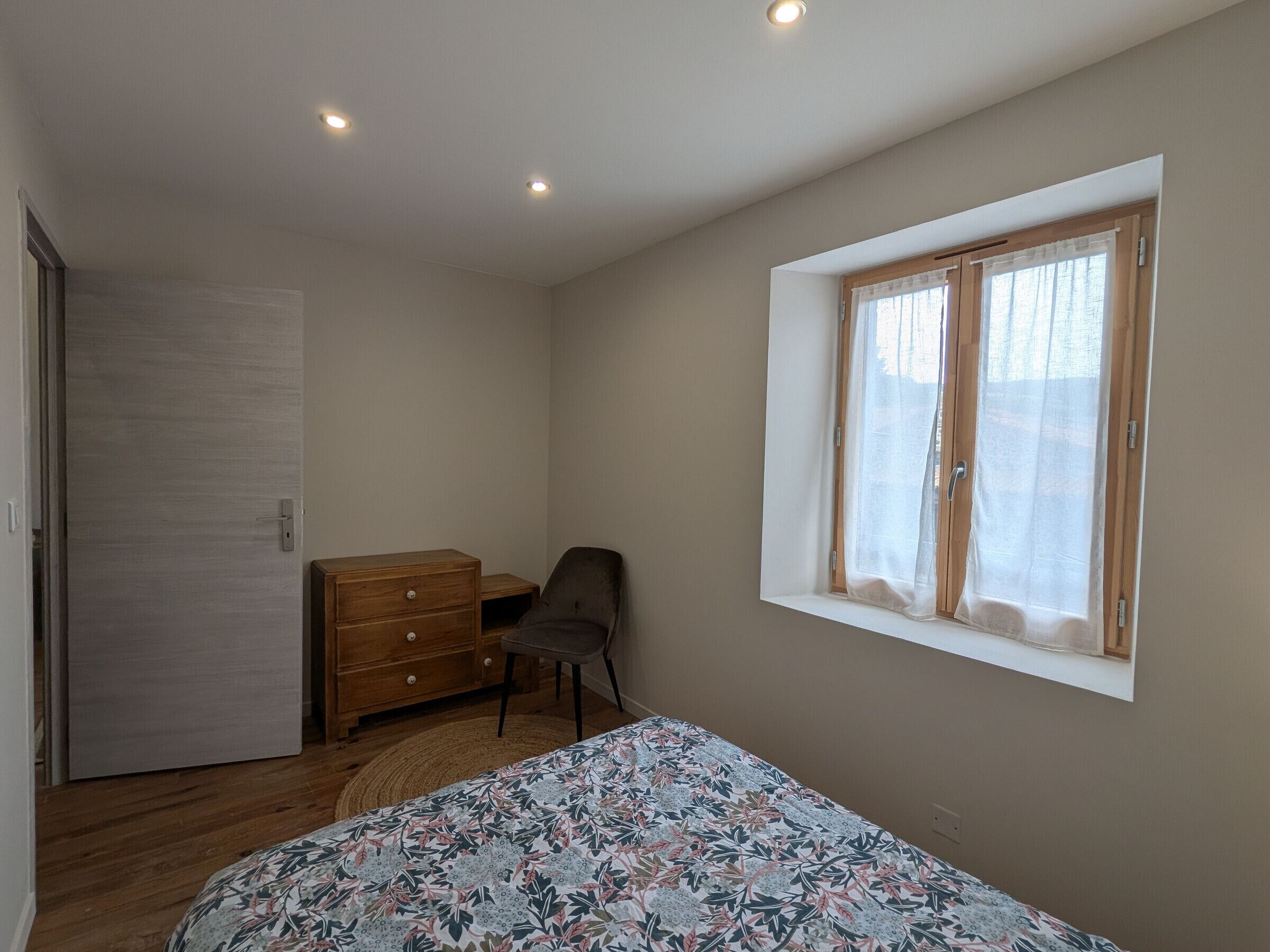 Une chambre à coucher avec un lit, une commode, une chaise, une fenêtre avec des rideaux et une porte.