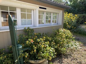 A house with a windowed porch, a green chair, and a garden with various plants and flowers.