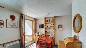 A dining area with a wooden table and chairs, a bookshelf, a television, and a mirror on the wall. - Studio 4 pax, south balcony, pets allowed, parking (Les Menuires)