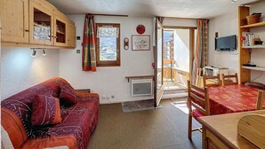 A cozy room with a wooden sofa, a dining table, and a view of a mountain landscape through a window. - Studio 4 pax, south balcony, pets allowed, parking (Les Menuires)