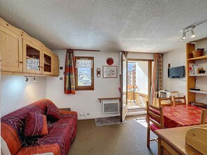 A cozy room with a wooden sofa, a dining table, and a view of a mountain landscape through a window. - Studio 4 pax, south balcony, pets allowed, parking (Les Menuires)