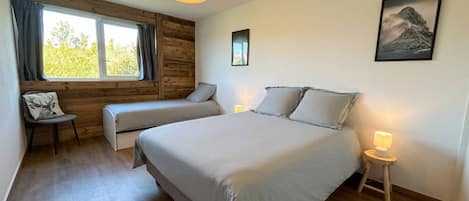 Un dormitorio con una cama grande, una silla con cojín, una mesita de noche con lámpara y una ventana con cortinas.