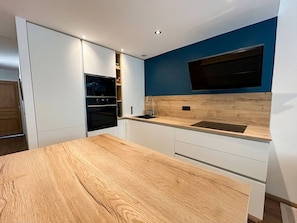 A compact kitchen with white cabinets, a wooden countertop, and a built-in oven.