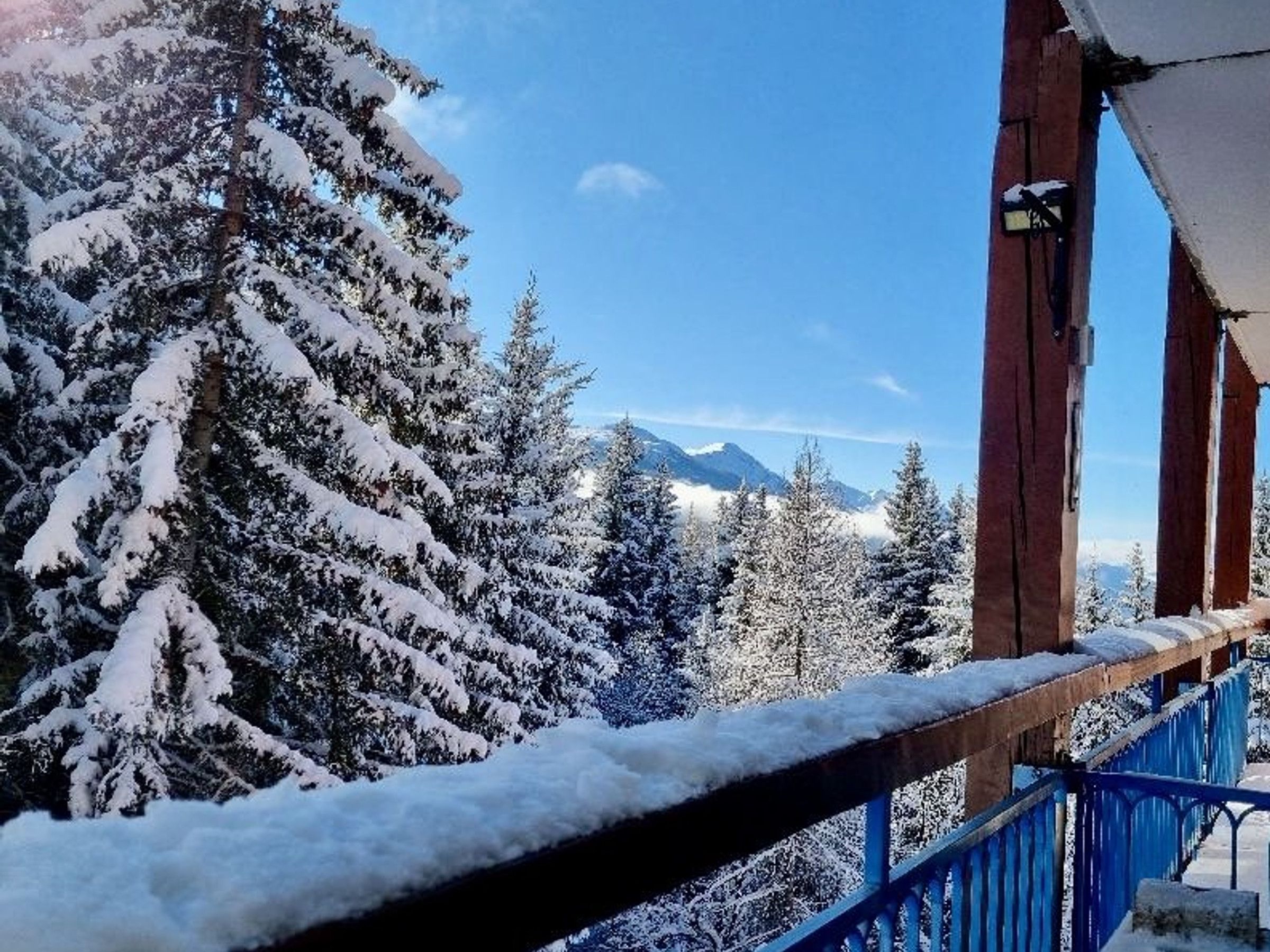 Un balcone imbiancato dalla neve con vista su alberi carichi di neve e montagne sullo sfondo.