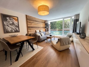 A modern living room with a wooden accent wall, a dining area, and a sofa set.