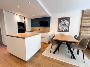 A modern kitchen with a central island, a dining area with a wooden table and chairs, and a mounted artwork on the wall.