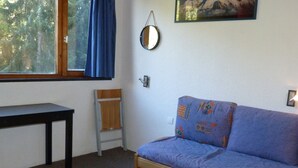Ein Zimmer mit einer hölzernen Sitzbank, einem blauen Sofa, einem kleinen Tisch, einem Fenster mit blauen Vorhängen, einem wandmontierten Spiegel und einem Gemälde.