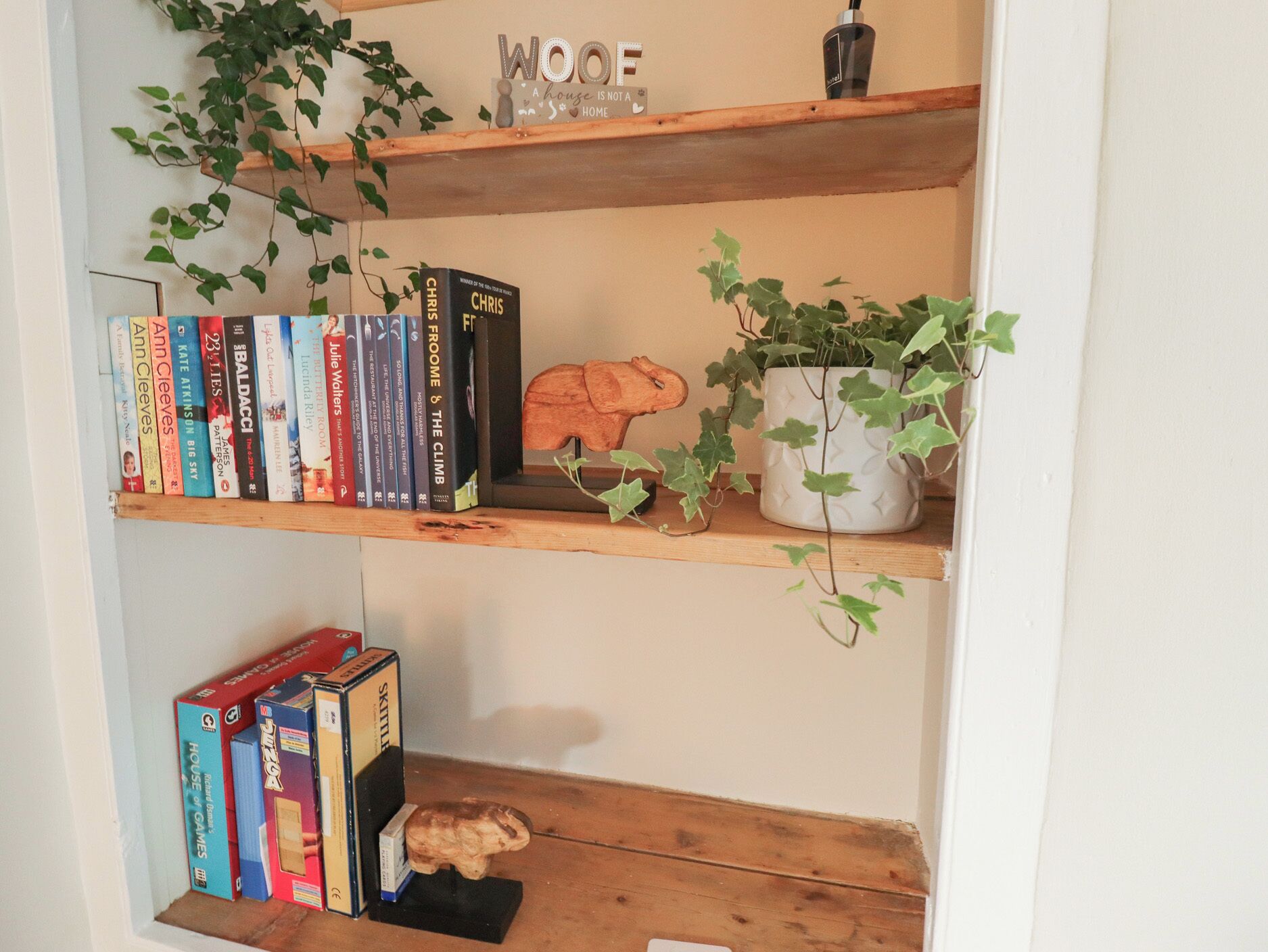 Uma estante com livros, uma pequena planta e uma escultura de madeira.