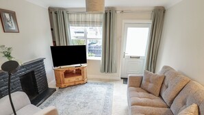 A living room with a fireplace, a television on a wooden stand, a beige sofa, and a patterned rug. - Conisholme (Grimsby)