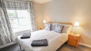 A neatly made bed with two pillows, two bedside lamps, and a window with curtains. - Conisholme (Grimsby)