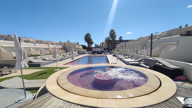A pool area with a circular water feature, lounge chairs, and umbrellas.