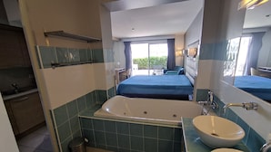 A modern bathroom with a large bathtub, two sinks, and a bed with a blue bedspread.