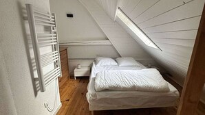 A small, cozy attic bedroom with a sloped ceiling, a single bed, a nightstand, and a wall-mounted radiator.