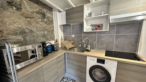 A compact kitchen with a stone wall, a built-in washing machine, a microwave, and a sink.
