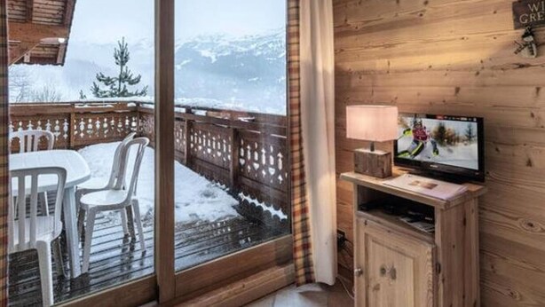 Een knus ogende kamer met een houten inrichting, een schuifdeur naar een balkon, een televisie, en een bordje met de tekst 'Welkom'.