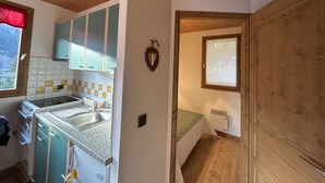 Een kleine keuken met een spoelbak, een fornuis en kastjes. Er is een raam met uitzicht op het omliggende landschap.